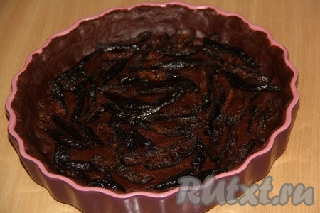 Достать форму с коржом из холодильника. Чернослив обдать кипятком, а затем нарезать на крупные кусочки. Выложить чернослив на дно формы.
