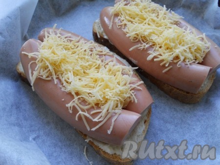 Бутерброды выложить на противень, застеленный пергаментом, и сверху сосиски посыпать твердым сыром, натертым на средней терке.
