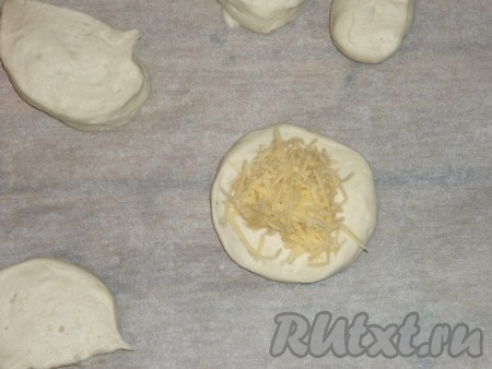 Сыр натереть на крупной тёрке. Каждую часть теста на припылённой мукой поверхности размять в лепёшку, на середину выложить по 1 столовой ложке с горкой сыра.