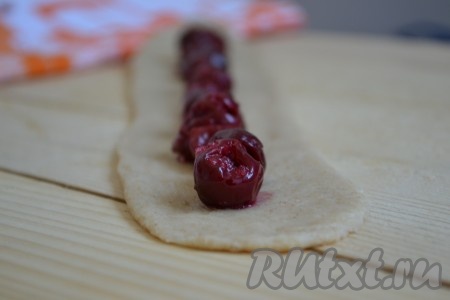 Каждый кусочек скатываем в колбаску и, на присыпанном мукой столе, раскатываем "язычок" длиной примерно 25 см, а шириной 7 см. По центру друг возле дружки выкладываем вишенки.
