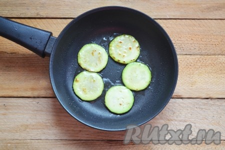 На сковороде разогреваем растительное масло, выкладываем в один слой кружочки кабачка. Обжариваем на среднем огне до подрумянивания с двух сторон. Обжаренные кабачки перекладываем на тарелку. Постепенно жарим все кабачки, добавляя в сковороду масло по мере необходимости. Даём жареным кабачкам остыть.