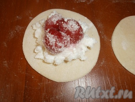 Берём два кружка для формирования одного вареника. В центр одного кружка кладём чайную ложку творога, сверху выкладываем 3 вишни, накрываем вторым кружком теста и скрепляем края кружков по кругу, формируя вареник.