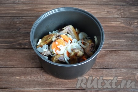 Выкладываем обжаренные кусочки курицы в чашу мультиварки, сверху добавляем лук, морковь и измельченные зубчики чеснока.
