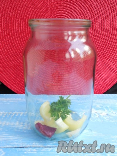 На дно стерилизованной банки поместить кусочек жгучего перца, немного сладкого перца, пару кусочков чеснока и пару веточек петрушки.