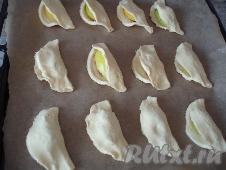 Получившуюся заготовку печенья выложить на противень, застеленный бумагой для выпечки. Постепенно сформировать всё творожное печенье в виде ракушек с начинкой из яблок и варёной сгущёнки. 