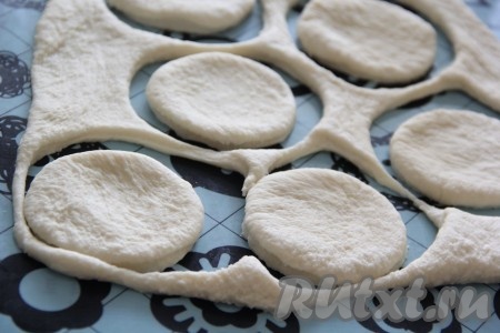 "Отдохнувшее" тесто на присыпанной мукой поверхности раскатать в пласт (тонко раскатывать тесто не нужно), а затем вырезать кружочки с помощью стакана или рюмки. Всё зависит от величины вашей формы.