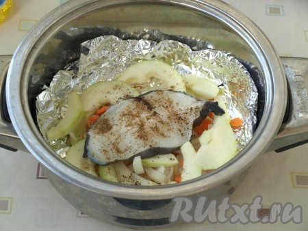 Сверху выложить размороженный, промытый и обсушенный стейк зубатки. Овощи и рыбу немного посолить сверху. Стейк приправить чёрным перцем и кориандром.
