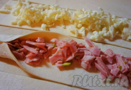 На 4 полоски по всей длине выложить сыр, немного отступив от краёв теста. На оставшиеся 4 полоски, немного отступив от краёв, по всей длине выложить колбасу. Защипнуть края полоски теста так, чтобы начинка оказалась внутри.