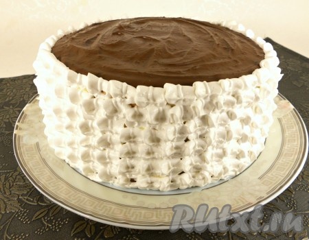Верх бисквитного торта покрыть растопленной шоколадной массой и дать застыть ей в холодильнике. Далее белковым кремом украсить бока торта с помощью кондитерского шприца или мешка с насадкой на ваше усмотрение.
