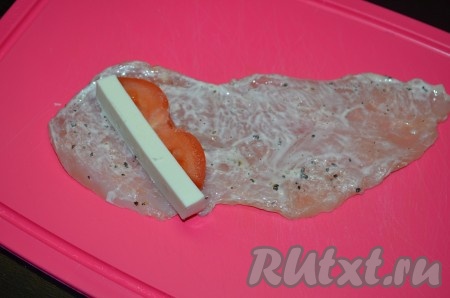 Берем пласт куриного филе, на край кладем по кусочку сыра и помидора, сворачиваем рулетиком. При желании можно скрепить край зубочисткой.
