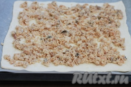 Первый пласт разморозившегося слоёного теста на присыпанной мукой поверхности раскатать до толщины 3 миллиметра, выложить на противень, застеленный бумагой для выпечки. На тесто выложить слой горбуши, отступая от краёв теста 1-1,5 сантиметра.