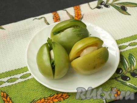 Вымыть зелёные помидоры и надрезать сбоку с одной стороны (получается как бы "книжка"). В разрез каждого помидора вложить небольшую веточку петрушки и пластинку чеснока.
