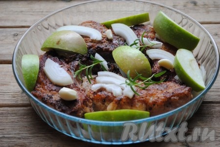 На мясо выложить очищенные зубчики чеснока, нарезанный полукольцами лук, веточки розмарина и яблоко, нарезанное дольками.&nbsp;
