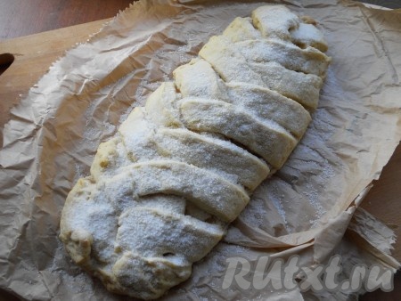 Верхнюю (узкую) часть "овала" подвернуть на начинку, затем, формируя плетёнку, как косичку, накрыть полосочками теста яблоки (берём полосочку справа, кладём на начинку, сверху накрываем полосочкой слева, снова берём полоску справа, а затем - слева, продолжая формировать плетёнку), нижнюю узкую часть овала тоже подвернуть на начинку. Таким же образом сформировать и второй пирог. Можно сделать и одну большую плетёнку. Перенести плетёнку вместе с пергаментом на противень и отправить в разогретую духовку. Выпекать творожную плетёнку с яблоками 30-40 минут при температуре 190-200 градусов. Готовую выпечку остудить, посыпать сахарной пудрой.