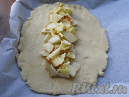 Разделить тесто на 2 части (то есть я формировала 2 творожных плетёнки). Вначале одну часть творожного теста раскатать в овал прямо на пергаменте. Яблоки нарезать на достаточно тонкие кусочки (я удалила из яблок только сердцевину, кожуру удалять не стала). Во всю длину по середине теста разместить половину нарезанных яблок (вторую половину яблок будем использовать для формирования второй плетёнки). Яблоки посыпать 0,5 чайной ложки цедры лимона (или корицы).