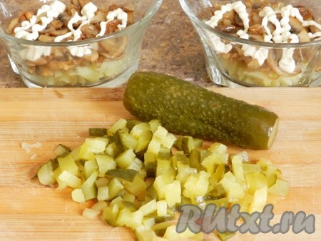 На слой картофеля выложить обжаренные шампиньоны с луком (несколько пластинок жареных шампиньонов отложите, чтобы в дальнейшем использовать для украшения салата), нанести сетку из майонеза. Солёные (или маринованные) огурцы нарезать на небольшие кубики и тоже равномерно разложить по креманкам поверх грибов.