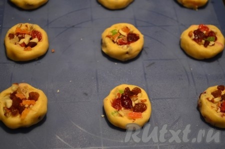 Сформировать из теста 24 шарика, разложить на расстоянии друг от друга на противне, застеленном пергаментом (или на силиконовом коврике), слегка приплюснуть. В образовавшееся небольшое углубление на поверхности каждого печенья разложить равномерно оставшуюся часть цукатов с орехами.