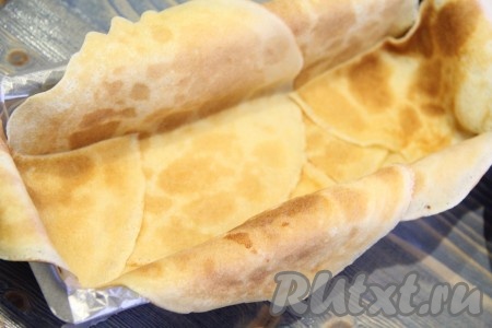 Прямоугольную форму для выпекания кексов или хлеба выстелить пищевой плёнкой так, чтобы края плёнки свисали с двух сторон формы (в конце приготовления свисающей плёнкой будем накрывать торт). Затем выложить блинчики внахлёст, края блинов должны свисать с формы (у меня ушло 4 блина плюс 1 блин на края). На дно формы выложить пару блинчиков, разрезанных пополам.