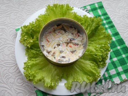 Далее на тарелке разместить листья салата, в середину поместить кулинарное кольцо и выложить до половины подготовленный салат, хорошо утрамбовывая его.