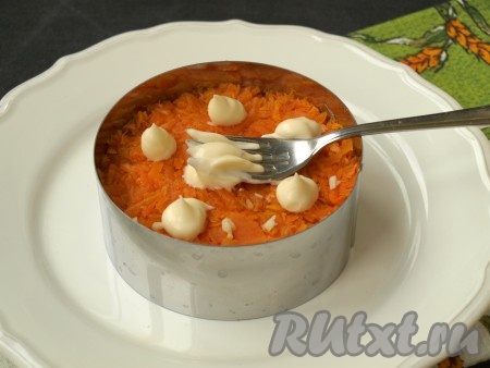 На тёрке натереть очищенную морковь, выложить её сверху мяса, добавить оставшийся пропущенный через пресс чеснок, смазать майонезом.
