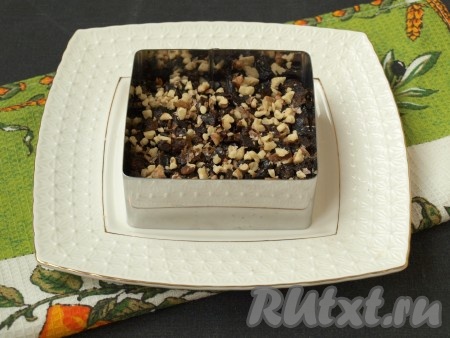 Чернослив промыть тёплой водой. Если чернослив суховат, его нужно переложить в небольшую ёмкость, залить кипятком, оставить минут на 5, затем слить лишнюю воду. Обсушить промытый (или запаренный) чернослив, выложив его на бумажное полотенце. Немного чернослива отложите для украшения салата. Нарезать оставшийся чернослив на небольшие кубики, равномерно разложить поверх филе. Порубить ножом грецкие орехи (2-3 ядра грецких орехов отложите для украшения) и посыпать хаотично сверху чернослива. Можно также перемешать орехи с черносливом. Этот слой можно смазывать майонезом, а можно и так оставить.