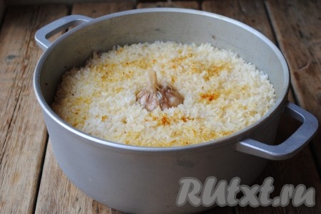 Варить плов из свинины на небольшом огне под крышкой до полного впитывания воды (около 20-30 минут). Готовый рис должен быть упругим, но не жестким внутри. Затем выложить чеснок в центр. Накрыть казан крышкой, хорошо укутать полотенцем и оставить на 20-30 минут для упаривания.
