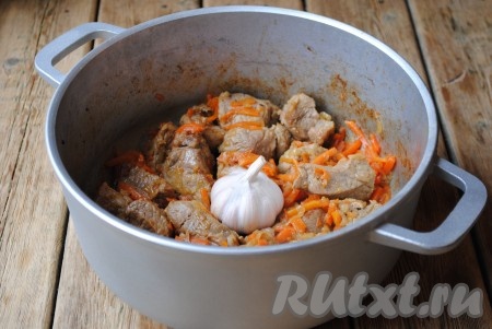 Перемешать и готовить ещё пару минут, затем добавить соль и приправу для плова. В центр выложить очищенный от верхней шелухи чеснок.
