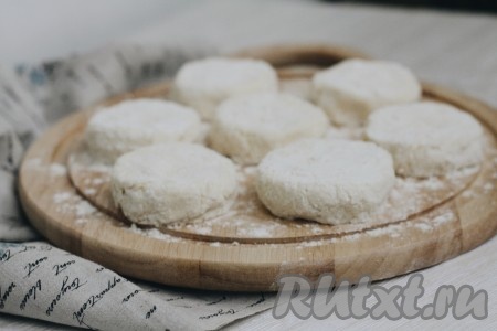 Из теста сформировать небольшие шарики, обвалять их в муке, а затем каждый шарик прижать сверху, чтобы получились лепёшки. Выложить сырники на разогретую с растительным маслом сковороду и обжарить на сильном огне с одной стороны до румяности, затем перевернуть, убавить огонь до средней температуры, накрыть крышкой и довести до готовности.