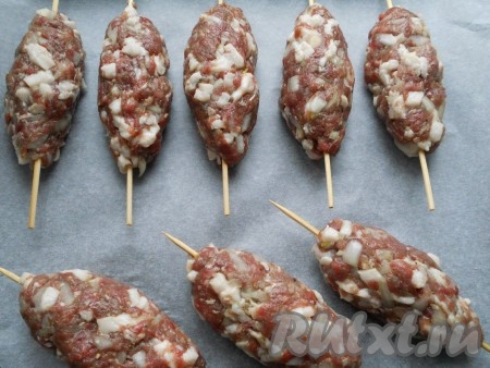Тщательно все перемешать. Вымешивать и отбивать фарш в течение 10 минут, пока он не станет вязким. Поместить фарш в холодильник на 30-40 минут. Деревянные шпажки замочить в холодной воде на 10 минут. Сформировать продолговатые котлеты, вставить шпажки, поплотнее прижимая мясо. Поместить люля-кебаб на противень, застеленный пергаментом.
