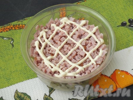 Далее нарезать на мелкие кубики ветчину, выложить сверху огурцов, немного прижать рукой и снова нанести майонез.