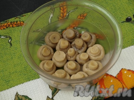 Для формирования салата лучше выбрать глубокую мисочку или контейнер с плоским дном. Застелить полностью дно и бока миски (или контейнера) куском пищевой плёнки, края плёнки должны свисать с краёв миски. Благодаря плёнке, переворачивать этот салат-перевёртыш будет достаточно просто. Я готовлю этот салат достаточно часто в одной и той же ёмкости, из неё салат достаётся хорошо, поэтому плёнкой я её не застилала. На дно миски плотно уложить шампиньоны шляпками вниз. Грибочки следует выбирать небольшие и желательно одного размера.