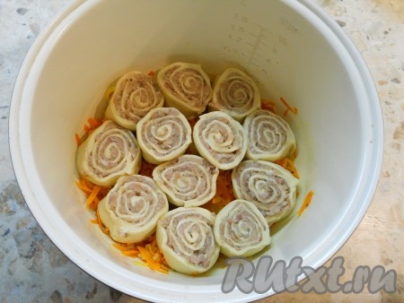 В чашу мультиварки влить растительное масло, добавить нарезанный репчатый лук и натертую на крупной терке морковь, выставить режим "Жарка" на 10 минут. Готовить овощи, помешивая, до сигнала. Рулет с мясом разрезать на 12 одинаковых частей, выложить рулетики горизонтально на овощную подушку.
