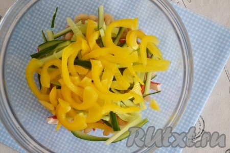 Перец вымыть и, удалив плодоножку и семена, нарезать тонкими ломтиками, выложить в салат к фасоли, крабовым палочкам и огурцам.
