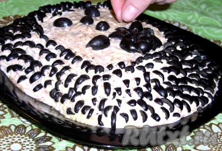 Верхний слой салата также смазать чесночно-ореховой заправкой и загладить поверхность широким ножом или лопаткой. Маслины нарезать тонкими, длинными полосками в форме колючек и выложить на салат. Из маслин вырезать глазки, носик "ежика" и оформить ими мордочку "ежика".