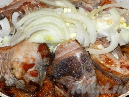 Добавить к мясу лук и чеснок, уменьшить огонь.