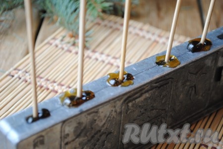 Разлить горячий сироп по углублениям в форме и вставить деревянные палочки.
