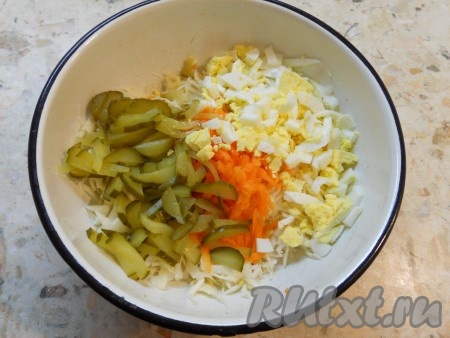 Очищенные рубленые вареные яйца и нарезанные небольшими кусочками соленые огурцы выложить в салат из свежей капусты и моркови.
