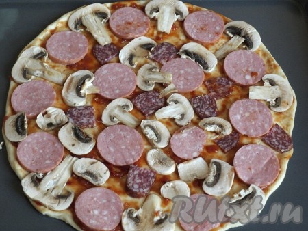 Нарезать колбасу и шампиньоны пластинками, красиво распределить на поверхности теста.
