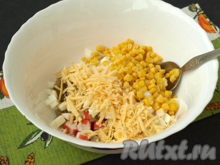 Твёрдый сыр натереть на крупной тёрке и вместе с консервированной кукурузой добавить в салат к яйцам, маринованным огурцам и крабовым палочкам.
