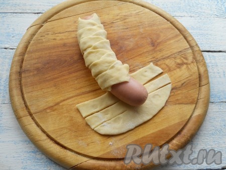 Завернуть сосиску полосками теста с каждой стороны поочередно (взять верхнюю полоску теста с одной стороны сосиски и выложить на сосиску, затем взять полоску с другой стороны и тоже выложить на сосиску поверх первой полоски и т.д.), чтобы получился вид косички.
