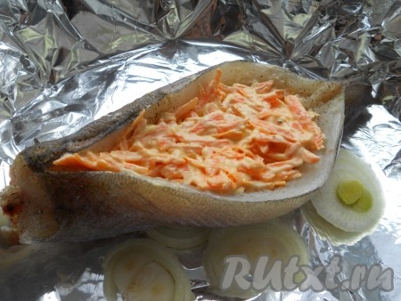 Форму застелить фольгой, выложить нарезанный кружками лук, полить растительным маслом, сверху - хек. Начинить рыбу морковью.

