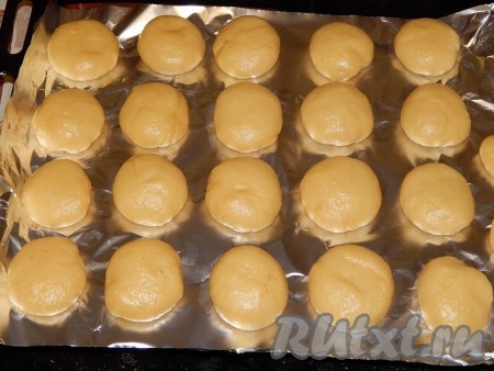 Прежде всего замесим песочное тесто для пирожного "Персики" . Для этого сливочное масло должно быть комнатной температуры, поэтому его заранее нужно достать из холодильника. В миску разбить яйца, всыпать сахар, взбить венчиком в течение 2-3 минут. Масса должна слегка посветлеть. В яично-сахарную смесь добавить мягкое сливочное масло, ванилин, сметану и ещё раз взбить венчиком. Затем добавить соду, погашенную уксусом, перемешать. Постепенно в яично-масляную смесь добавить муку, замешивая эластичное, мягкое, не липнущее к рукам тесто. Вначале собрать тесто в шар, а затем сформировать из него колбаску, нарезать её на 22 кусочка. Каждый кусочек теста скатать в шарик, слегка приплюснуть сверху (это будут половинки наших будущих персиков), выложить на противень, застеленный фольгой (или пергаментом). Выпекать 20 минут в духовке, разогретой до 200 градусов.