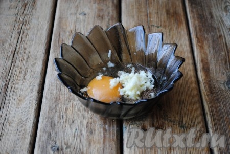 В отдельную тарелку вбить яйцо, добавить соль, чёрный молотый перец, приправу к мясу и пропущенный через пресс чеснок, хорошо перемешать с помощью вилки. 