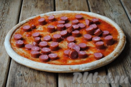 Охотничьи колбаски нарезать кружочками и равномерно распределить по всей основе. 