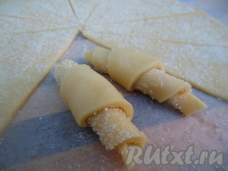 Разделите раскатанное тесто на 12 сегментов и, начиная от широкого края, скатайте каждый сегмент в рогалик.&nbsp; Аналогично по очереди раскатайте оставшиеся части теста, разделите раскатанные части на сегменты и сформируйте рогалики. Всего у вас получится 48-50 рогаликов. Сверху каждый рогалик обмакните в сахар.
