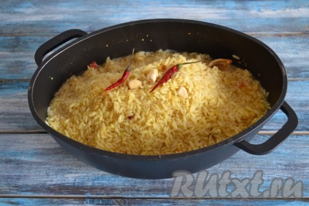 Затем рис собрать горкой, выложить целые очищенные зубчики чеснока и стручки острого перца, накрыть казан крышкой и оставить на слабом огне еще на 10 минут.
