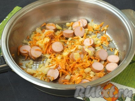 Кружочками нарезать сосиски, добавить их к обжаренным овощам, готовить ещё несколько минут, иногда перемешивая.
