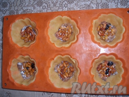 На дно каждой формочки положить кусочек фольги и насыпать сухую фасоль (или горох).