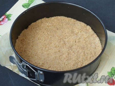 Дно формы (у меня форма диаметром 22 см) проложить пергаментом, выложить крошку, хорошо утрамбовать и на 30 минут убрать в холодильник.
