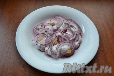 Полить редис частью заправки. Затем сверху выложить слой нарезанного тонкими полукольцами фиолетового лука.
